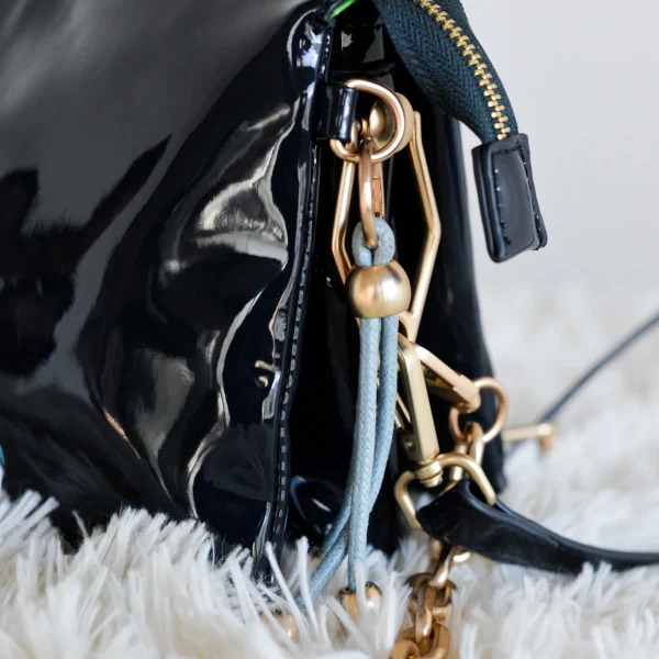 Diseño estructurado, brillo elegante y ese toque Agatha que la hace única. Esta bandolera de charol con formato acordeón es el bolso ideal para quienes buscan orden y estilo en un solo accesorio. Cuenta con varios compartimentos independientes, perfectos para organizar tus esenciales sin perder tiempo. En el frontal, el logo en contraste aporta color y personalidad, mientras que los pompones decorativos tipo llavero suman un detalle divertido y distintivo. Incluye dos tipos de asas: una cadena corta metálica para llevar al hombro y una correa larga de charol ajustable para usarla como bandolera. Tú decides cómo llevarla según el plan. Medidas: 16*14*12