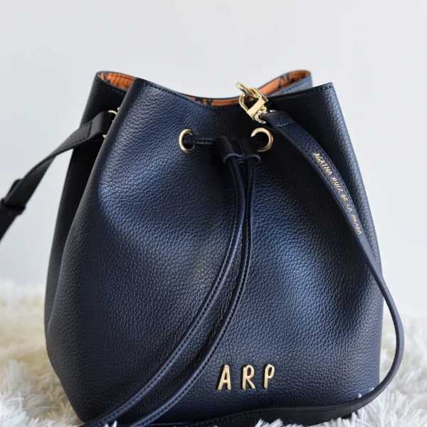 Este bolso bombonera de piel vegana es la mezcla perfecta entre diseño actual y funcionalidad. Su formato redondeado y suave le da un aire sofisticado pero relajado, ideal para looks de día o de noche. El interior sorprende con el nylon estampado a contraste, sello distintivo de la colección, y un compartimento central con cremallera para organizar tus imprescindibles con seguridad. Además, incluye correa larga ajustable, para que puedas llevarlo como bandolera o al hombro, según el momento. Medidas: 22*23*16