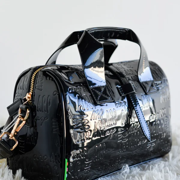 Compacto, estructurado y con mucha personalidad: este bolso bowling es el aliado perfecto para tu día a día con un toque de sofisticación.Fabricado en charol estructurado con el logo ARP grabado, combina textura y brillo en un diseño cómodo y funcional. Su cremallera superior garantiza seguridad, y la correa incluida te permite llevarlo al hombro o cruzado según lo necesites. Su formato redondeado aporta ese aire retro que nunca pasa de moda, reinventado con el estilo inconfundible de Agatha Ruiz de la Prada. Medidas: 28*20*10