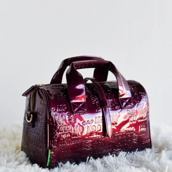 Compacto, estructurado y con mucha personalidad: este bolso bowling es el aliado perfecto para tu día a día con un toque de sofisticación.Fabricado en charol estructurado con el logo ARP grabado, combina textura y brillo en un diseño cómodo y funcional. Su cremallera superior garantiza seguridad, y la correa incluida te permite llevarlo al hombro o cruzado según lo necesites. Su formato redondeado aporta ese aire retro que nunca pasa de moda, reinventado con el estilo inconfundible de Agatha Ruiz de la Prada. Medidas: 28*20*10