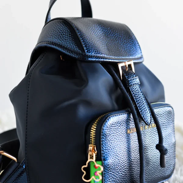 Diseño funcional y estilo contemporáneo se unen en esta mochila mediana de la colección. Con un formato práctico que incluye tapa superior y un bolsillo delantero en piel sintética metalizada, combina resistencia y sofisticación en un solo accesorio.Las correas de algodón ajustables garantizan comodidad y adaptabilidad para llevarla todo el día sin esfuerzo. Además, los detalles en dorado y el icónico tirador con la nube realzan su carácter exclusivo. Ideal para quienes buscan una mochila ligera pero con personalidad. Medidas: 21*26*11