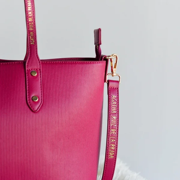 Este bolso shopper es la definición perfecta de fondo de armario con carácter. De diseño limpio y líneas depuradas, está confeccionado en piel vegana grabada con efecto rayado vertical, lo que le da textura y un aire sofisticado. Su amplio formato lo convierte en el compañero ideal para el día a día, con cremallera superior para mantener todo seguro. En la parte frontal, destacan las iniciales ARP en metal dorado, mientras que el logo de Agatha Ruiz de la Prada aparece en el asa y la correa, aportando un toque distintivo y elegante. Medidas: 35*26*12