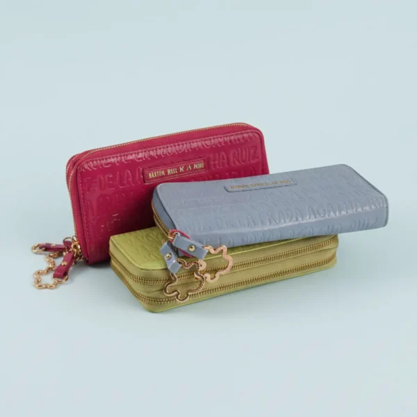 Este billetero grande de Agatha Ruiz de la Prada combina diseño, color y funcionalidad en un formato espacioso y muy práctico. Confeccionado en charol brillante en tonos pastel, el logo de la marca grabado en toda la superficie aporta un acabado elegante y texturizado, reforzando el estilo inconfundible de la firma. Cuenta con dos compartimentos independientes con cremallera, lo que permite organizar tarjetas, billetes y monedas de forma segura y cómoda. Los tiradores incluyen el icónico icono de Agatha, añadiendo un detalle distintivo y divertido que caracteriza a la colección. Un billetero ligero, resistente y muy versátil, perfecto para uso diario o como complemento a juego con los bolsos y monederos de la misma línea. Ideal para quienes buscan organización sin renunciar al estilo y color de Agatha Ruiz de la Prada. Medidas: 20*10*4