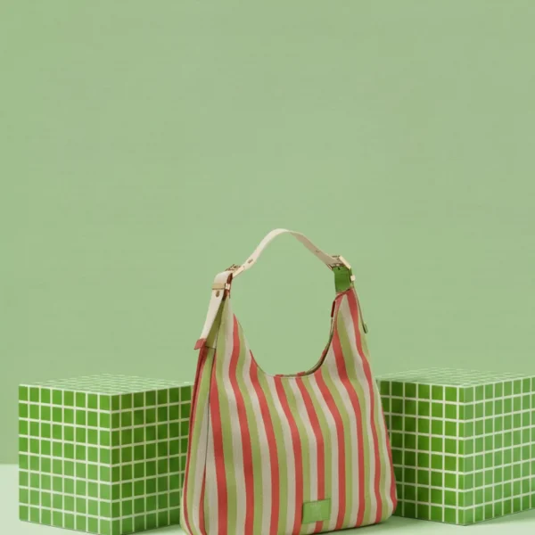 Este bolso hobo forma parte de la colección en lona gruesa de líneas de color, un tejido resistente que combina el verde con tonos vibrantes como  rosa fucsia. Su diseño es amplio, ligero y muy cómodo, perfecto para quienes buscan un bolso práctico con un estilo veraniego y actual. El modelo incorpora un asa regulable de algodón en tono crema, suave al tacto y con un aire natural que equilibra perfectamente la intensidad del estampado. Esta asa permite ajustar la altura del bolso para llevarlo al hombro con total comodidad. Los detalles metalizados aportan un toque moderno que complementa el look fresco del tejido, creando un diseño equilibrado entre lo casual y lo chic. Su formato hobo ofrece buena capacidad sin perder forma, ideal para el día a día, viajes o planes en los que necesitas un bolso amplio pero cómodo. Medidas: 32*25*9