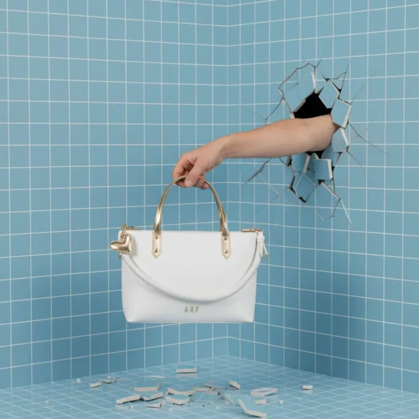 El shopper de la colección de Agatha Ruiz de la Prada es ese bolso amplio y estiloso que funciona igual de bien para el día a día que para ocasiones más especiales. Está confeccionado en piel vegana de alta calidad, suave, resistente y con un acabado muy limpio. Incluye cremallera superior, perfecta para llevar todo bien protegido. En el frente destaca el asa corta decorativa, elaborada en un cordón de la misma piel, un detalle original y característico de la colección. Los detalles metalizados aportan ese punto chic que eleva el diseño sin perder la esencia práctica del formato shopper. Y, como toque final, lleva un llavero con el icónico corazón de Agatha Ruiz de la Prada, un elemento reconocible y alegre que suma personalidad al bolso. Un shopper espacioso, moderno y muy ponible, perfecto para quienes buscan estilo y comodidad en un solo accesorio. Medidas: 34*26*10