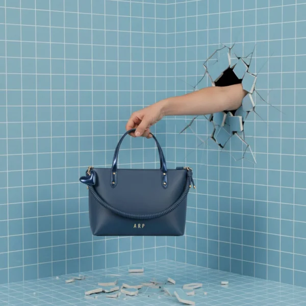 El shopper de la colección de Agatha Ruiz de la Prada es ese bolso amplio y estiloso que funciona igual de bien para el día a día que para ocasiones más especiales. Está confeccionado en piel vegana de alta calidad, suave, resistente y con un acabado muy limpio. Incluye cremallera superior, perfecta para llevar todo bien protegido. En el frente destaca el asa corta decorativa, elaborada en un cordón de la misma piel, un detalle original y característico de la colección. Los detalles metalizados aportan ese punto chic que eleva el diseño sin perder la esencia práctica del formato shopper. Y, como toque final, lleva un llavero con el icónico corazón de Agatha Ruiz de la Prada, un elemento reconocible y alegre que suma personalidad al bolso. Un shopper espacioso, moderno y muy ponible, perfecto para quienes buscan estilo y comodidad en un solo accesorio. Medidas: 34*26*10