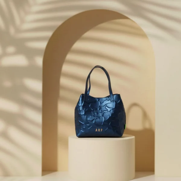 Este bolso tote de Agatha Ruiz de la Prada está diseñado en piel sintética metalizada, con un acabado elegante y luminoso que aporta un toque sofisticado a cualquier look. El material incorpora los iconos de la marca grabados con volumen, creando un efecto en relieve que añade textura y personalidad al diseño. El bolso incluye un neceser interior con cremallera, ideal para organizar y proteger los objetos más pequeños. Además, cuenta con un cierre interior, que aporta un extra de seguridad sin perder comodidad. Su formato tote es amplio y práctico, perfecto para el uso diario, trabajo o planes en los que necesitas más capacidad. Un modelo funcional y elegante que combina diseño, organización y la identidad inconfundible de Agatha Ruiz de la Prada. Medidas: 27*28*13