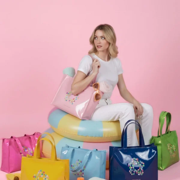 Esta bolsa tote de charol de Agatha Ruiz de la Prada combina funcionalidad y diseño en un formato rectangular elegante y muy versátil. Confeccionada en charol blandito, ofrece un tacto suave y flexible que aporta comodidad sin perder estructura. El frontal está decorado con el icónico estampado de la flor de Agatha Ruiz de la Prada, uno de los símbolos más reconocibles de la firma, aportando personalidad y un toque distintivo al diseño. Su acabado brillante eleva cualquier look, convirtiéndola en una opción perfecta tanto para el día a día como para ocasiones más especiales. Cuenta con cierre de cremallera superior, ideal para llevar tus pertenencias con mayor seguridad, y un interior completamente forrado que aporta un acabado cuidado y funcional. Gracias a su formato amplio, es perfecta para acompañarte en jornadas largas, trabajo, recados o como bolso principal diario. Un tote práctico, cómodo y con el estilo inconfundible de Agatha Ruiz de la Prada. Medidas: 34*27*11